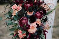 a luxurious fall wedding bouquet of pink, fuchsia, deep purple and black blooms, berries and greenery plus ribbons for a decadent bridal look
