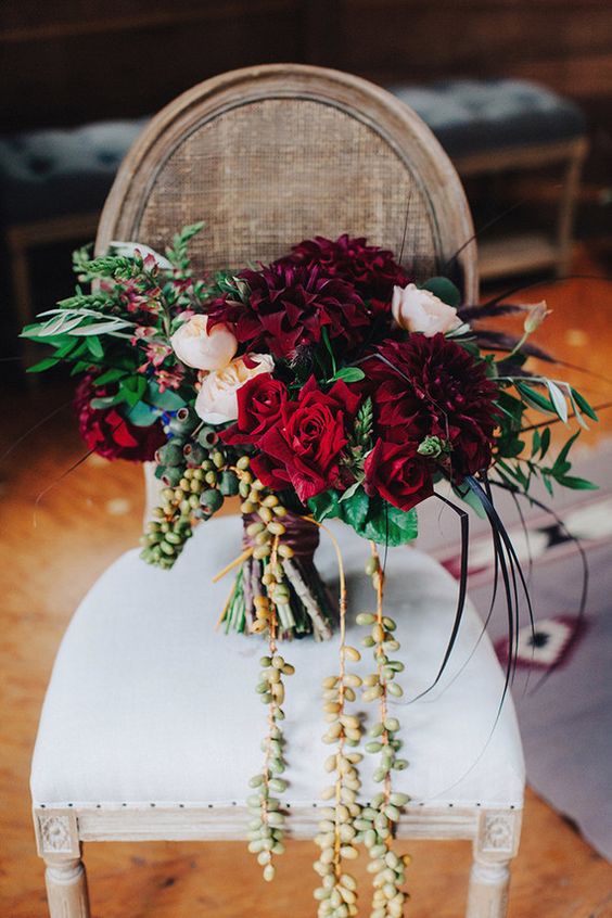 a luxurious wedding bouquet with berries hanging down, burgundy and blush blooms and foliage