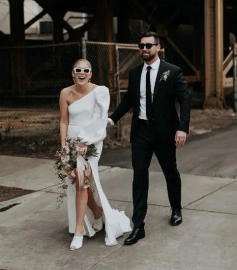 a modern plain one shoulder puff sleeve wedding dress with a slit and a train, white mules and pearl earrings