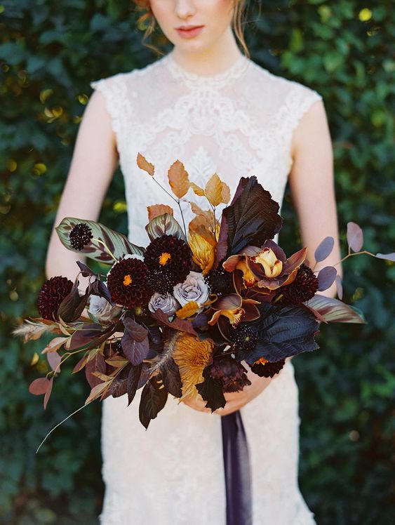 a moody and luxurious fall wedding bouquet with dark leaves, blooms, touches of mustard and rust, dried leaves and some herbs