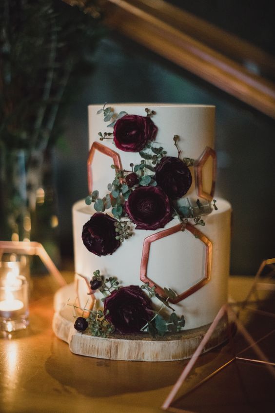 a moody fall wedding cake with copper hexagons and greenery and purple blooms looks amazing
