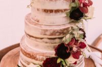 a naked wedding cake decorated with burgundy and white blooms and foliage for a brighter look