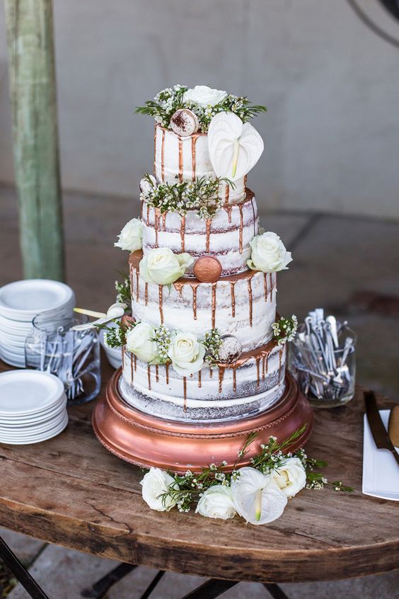 a naked wedding cake with copper drip, greenery and white blooms plus copper macarons