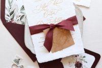 a neutral and gold wedding invitation suite with bold burgundy envelopes with a floral lining