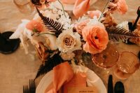 a pretty modern wedding tablescape with a rust, blush and orange floral centerpiece, rust napkins and menus, black cutlery