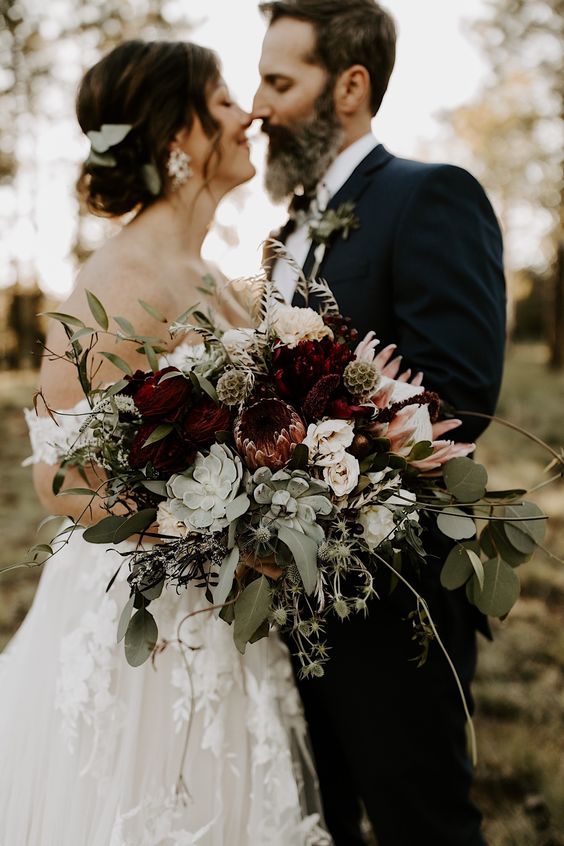 a refined fall wedding bouquet of white, burgundy and pink flowers, greenery, thistles, a succulent and berries is a classy idea for the fall