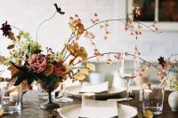 a refined fall wedding centerpiece of a bowl, greenery and foliage, blooming branches and dark blooms
