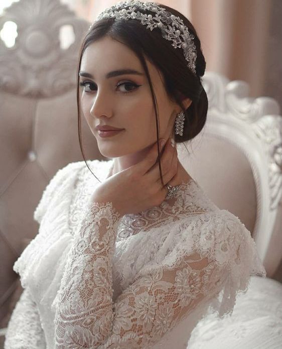 a refined vintage lace A-line wedding dress with a high neckline, a ruffle, long sleeves, an embellished headpiece and statement earrings