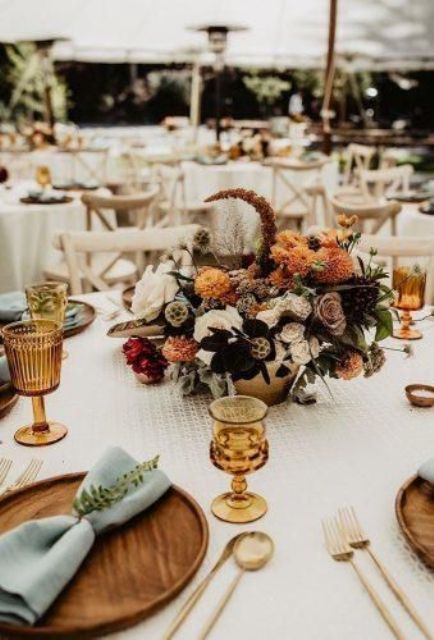 a refined wedding table setting with amber goblets, wooden plates, gold cutlery and rust and amber blooms