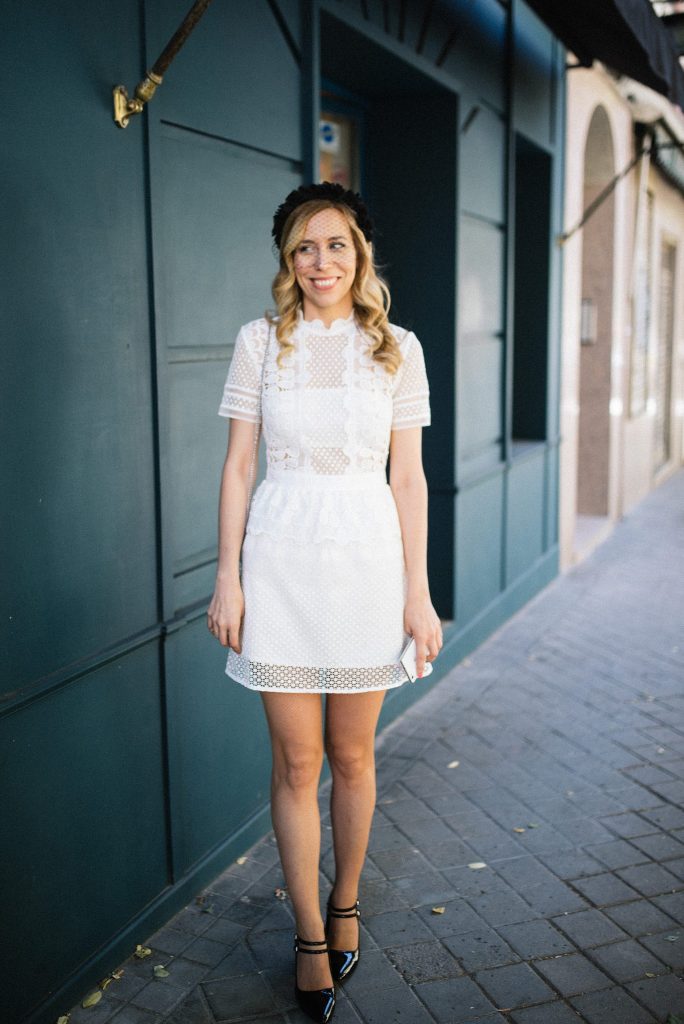 a retro-loving bride in a mini polka dot dress with illusion parts, short sleeves and a ruffle neckline, a black headpiece with a veil and black shoes