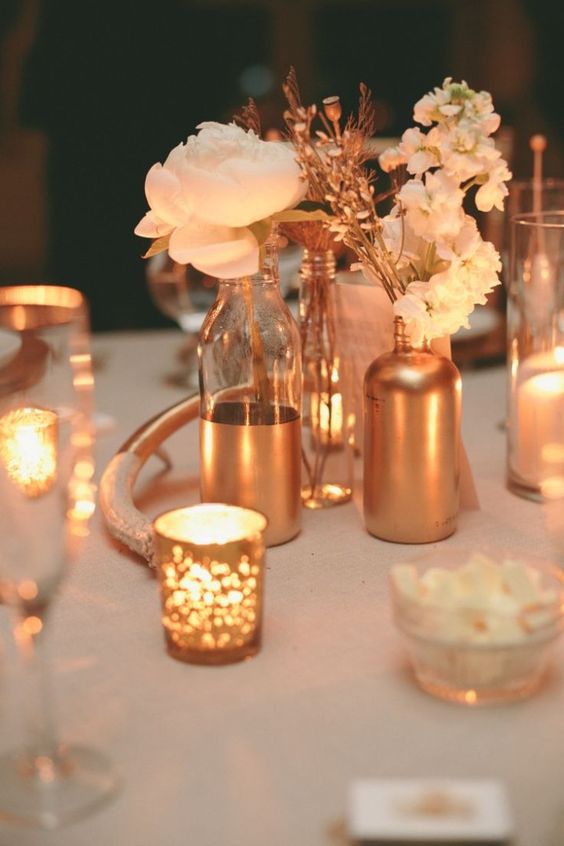 a romantic and glam wedding centerpiece of copper bottles and vases, blush blooms and copper candleholders