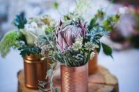 a rustic wedding centerpiece of a wood slice, copper and gold tin cans, greenery and neutral and pink blooms