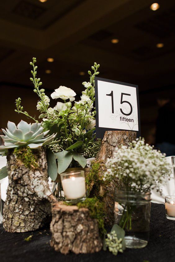 a rustic wedding centerpiece of tree stumps with white blooms, succulents, candles and a modern table number