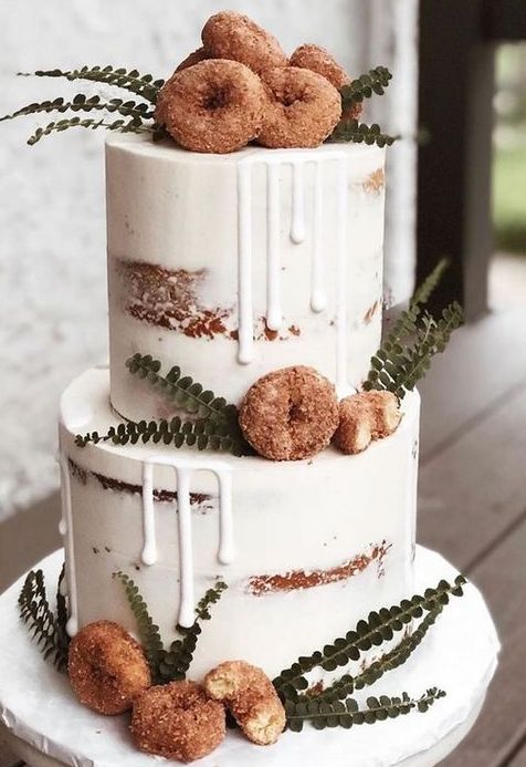 a semi naked fall wedding cake decorated with white drip, greenery and donuts looks delicious