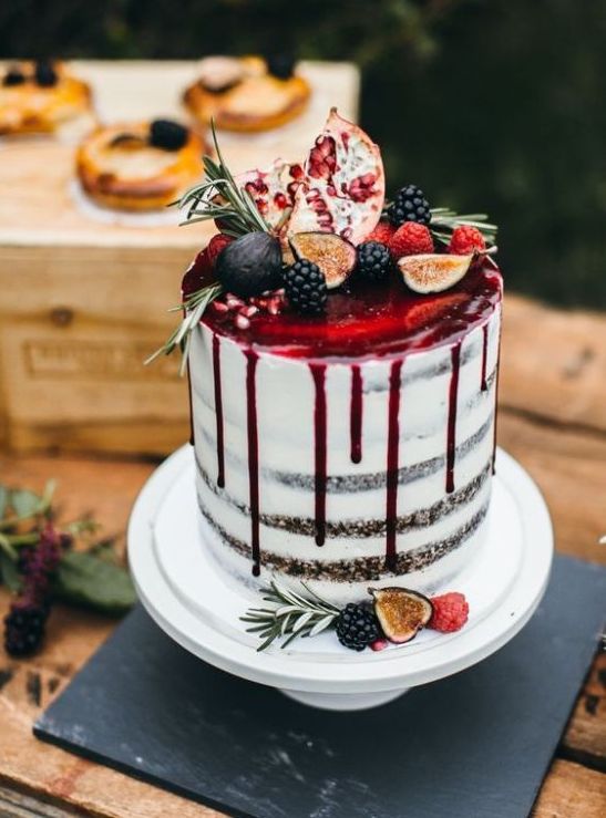 a semi naked wedding cake with pomegranate drizzle, blackberries and figs and some greenery on top