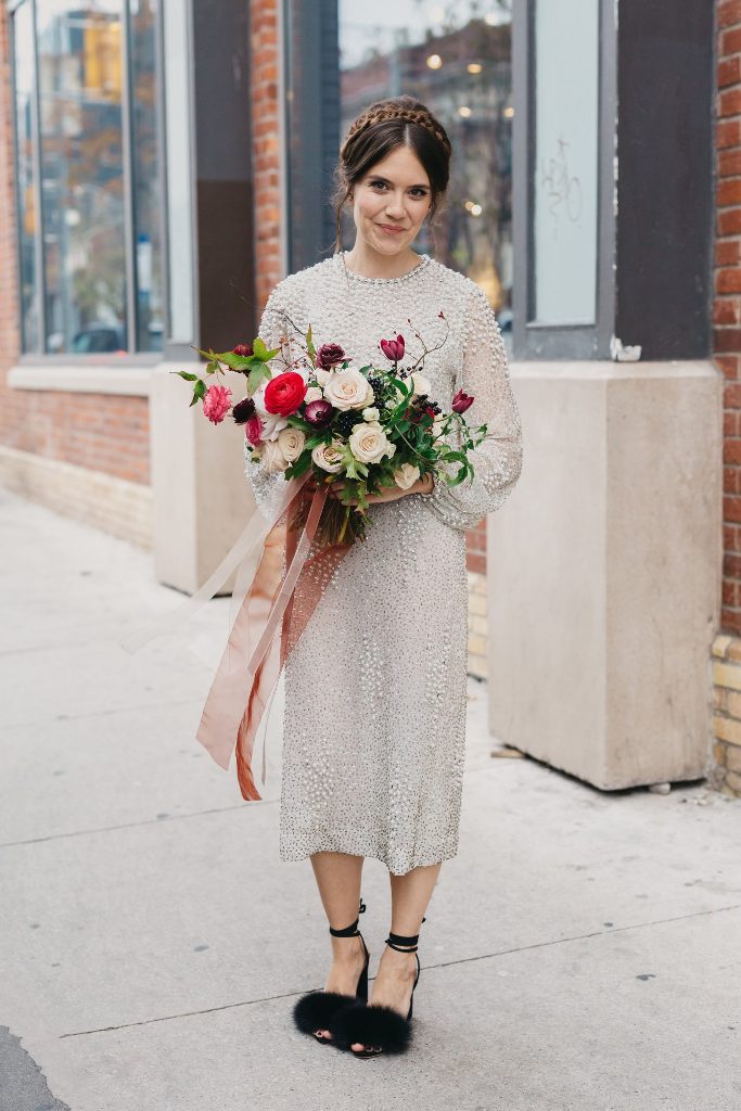 a shiny and boldly embellished midi silver wedding dress with a high neckline, long sleeves and fluffy black shoes