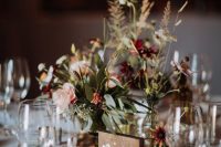 a simple and relaxed fall wedding centerpiece with a cluster of vases, greenery, burgundya dn pink blooms and a wooden table number
