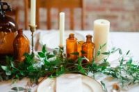 a simple tablescape with greenery, amber bottles, neutral candles and elegant cutlery and plates