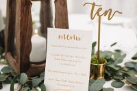 a simple wedding centerpiece of greenery, a wooden candle lantern, a calligraphy table number in a shot with moss