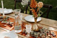 a simple yet chic fall wedding tablescape with a rust runner, rust blooms and cards, white porcelain and candles