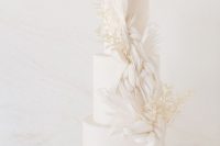 a sophisticated wedding cake with sugar feathers and white dried leaves is a refined dessert