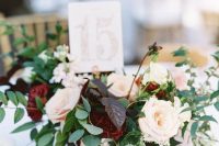 a sophisticated wedding centerpiece of blush and burgundy blooms, foliage and dark leaves and a table number