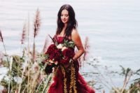 a strapless burgundy mermaid wedding dress with draperies and a cascading wedding bouquet with greenery and burgundy blooms
