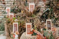 a stylish boho fall wedding seating chart done of rattan and wicker ottomans, dried grasses and blooms and cards displayed
