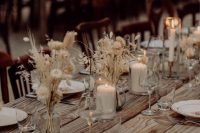 a stylish boho fall wedding tablescape with an uncovered table, dried blooms and grasses and candles plus neutral napkins
