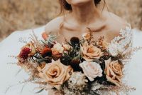 a stylish fall wedding bouquet of blush, rust, burgundy, deep purple, greenery, dried foliage and with long ribbons is cute and chic