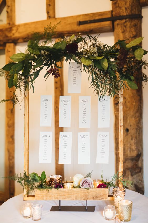 a stylish fall wedding seating chart with greenery, bright blooms, candles, himmeli and floating papers