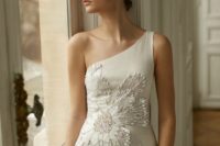 a stylish one shoulder wedding dress with a bold rhinestone flower applique over the whole bodice and partly over the skirt plus a thigh high slit