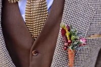 a stylish tweed suit, a brown waistcoat, a blue shirt, a printed bow plus a berry and flower boutonniere