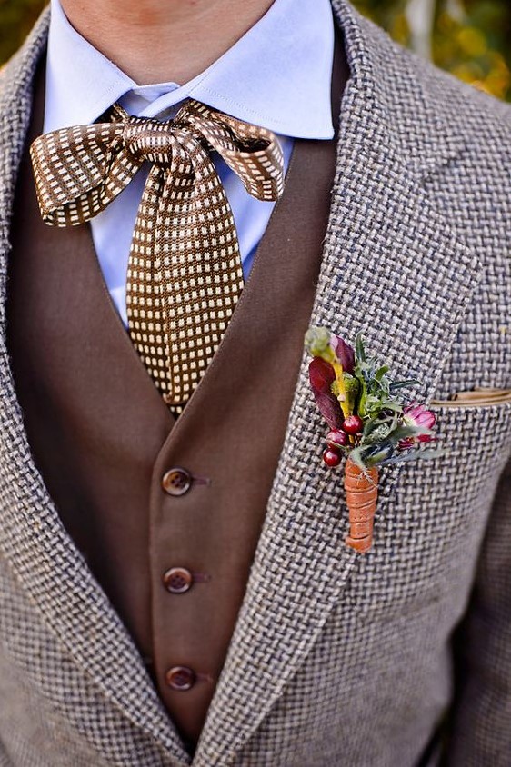 a stylish tweed suit, a brown waistcoat, a blue shirt, a printed bow plus a berry and flower boutonniere