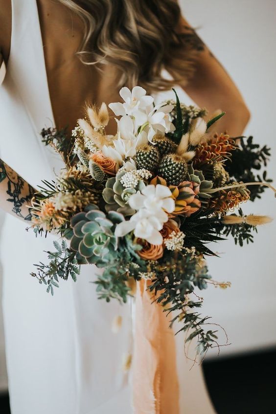 a textural and dimenstional wedding bouquet with white and orange blooms, succulents, cacti, grasses and peachy ribbons