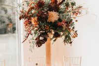 a textural tall floral centerpiece in a copper vase, with lots of various greenery, rust and burgundy blooms and dark foliage
