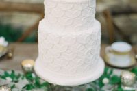a textural white wedding cake with a floral pattern and a white white bloom on top looks vintage-like and chic