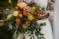 a vibrant fall wedding bouquet of pink, yellow, orange blooms, greenery, billy balls and even a yellow pinecone with cascading touches