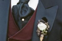 a vintage boutonniere of a white rose, some berries, dark foliage and feathers plus button accents for a vintage or steampunk wedding
