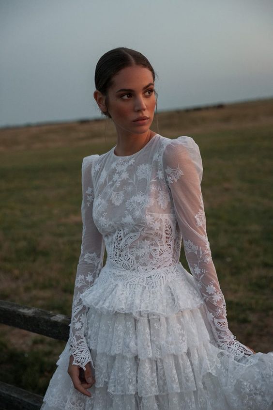 a vintage inspired and granny chic A line wedding dress of lace, with puff sleeves, a high neckline and a ruffle tiered skirt