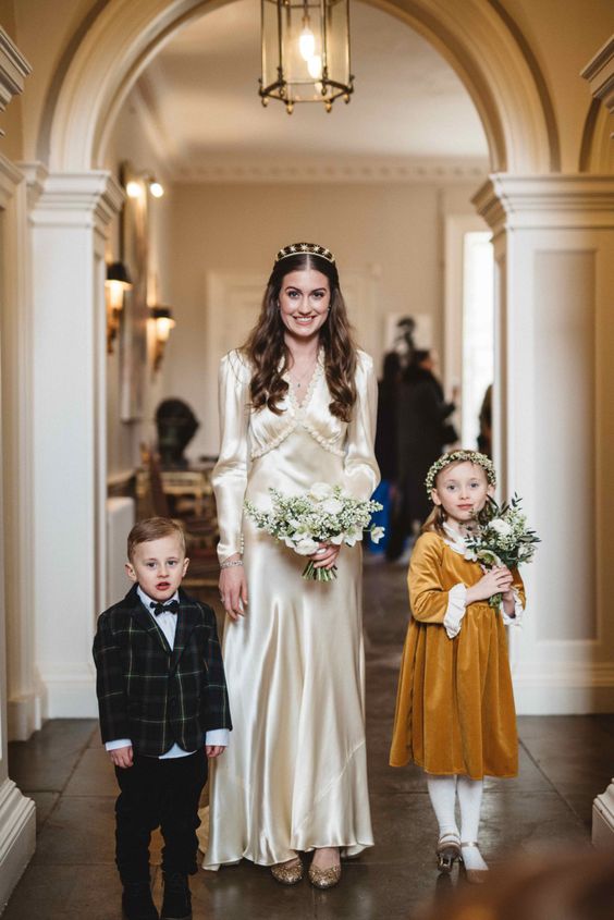 a vintage-inspired champagne-colored wedding dress with long sleeves, a V-neckline, gold shoes and an embellished headband