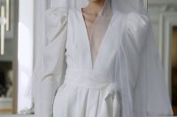 a vintage-inspired plain wedding dress with a plunging neckline, puff sleeves, a pleated skirt, a sash and a veil plus statement earrings