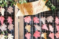a wedding seating chart of bright paper leaves, greenery and a banner is a nice idea for a fall wedding that you can DIY