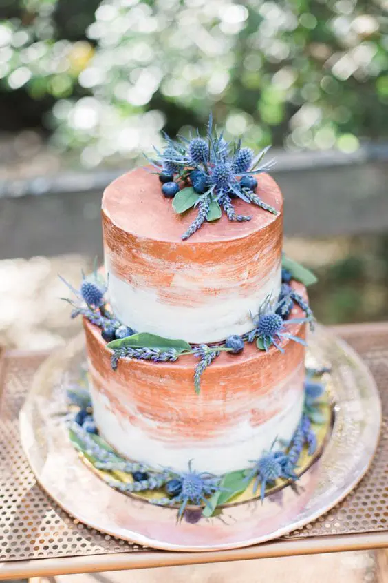 a white and copper brushstroke wedding cake with greenery, berries and thistles is very bold
