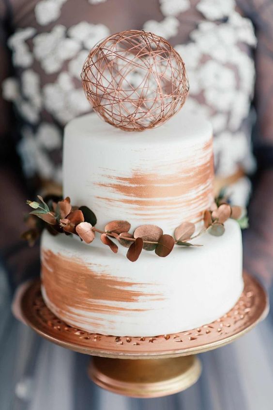a white and copper wedding cake with copper leaves, a wire ball and copper brushstrokes is very bold