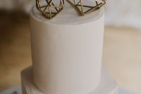 a white geometric wedding cake with gold himmeli toppers and greenery and white blooms