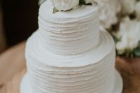 a white textural wedding cake with stripes, white blooms and a gold calligraphy topper