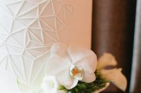 a white wedding cake with geometric patterns, white orchids and greenery is very elegant