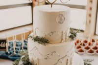 a white wedding cake with mountains painted, a cute topper and some fir branches is very lovely