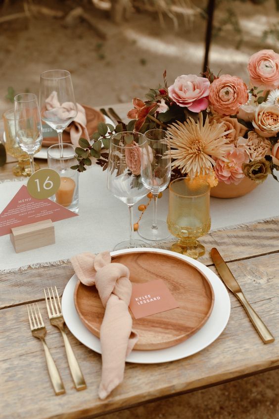 an earthy-colored fall wedding tablescape with neutral linens, woodne plates, a bright floral centerpiece and pink wedding stationery